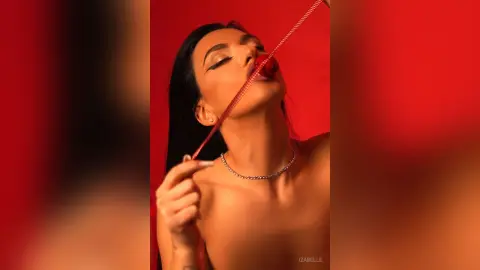 Iza — Glamorous woman with dark hair wearing a silver necklace posing against a bold red background.