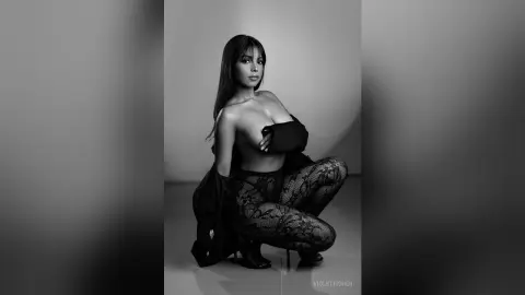 Glamorous woman in black lace bodysuit and patterned tights posing in a moody black and white studio portrait.