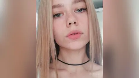 Blonde woman with freckles and winged eyeliner wearing a black choker in a soft, natural light portrait.