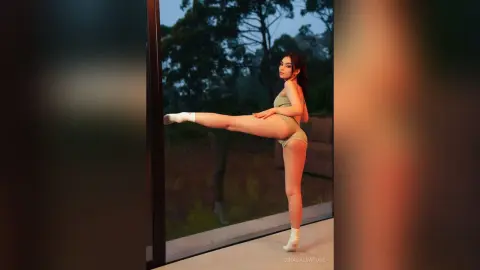 GinaSalvatore stands sideways against a glass window, wearing a light green bodysuit and white socks.