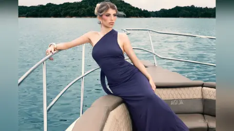 Elegant woman in a navy blue halter gown relaxing on a luxury boat on a calm lake at sunset.