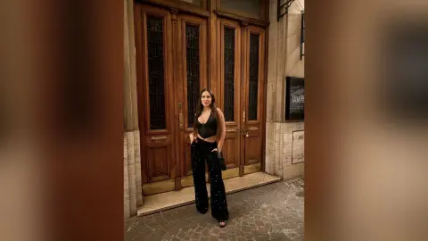 Stylish woman in a black crop top and wide-leg trousers standing before ornate wooden doors in a classic setting.