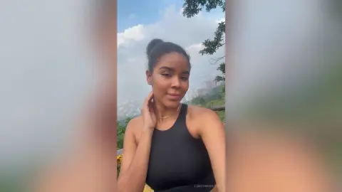 LoreyHamilton — Young woman in a black tank top smiling during a scenic outdoor hike under a blue sky.