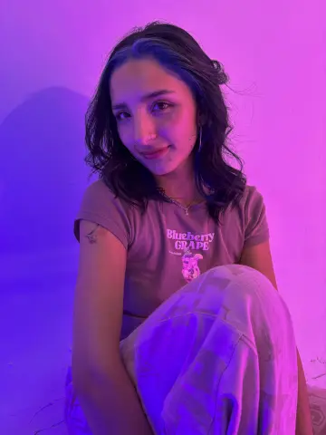 Young woman in a graphic t-shirt sitting in dreamy purple neon lighting with a relaxed mood.