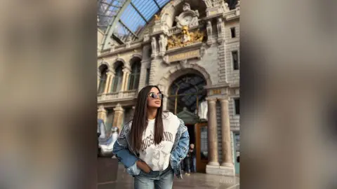Stylish woman in denim jacket and sunglasses standing before grand classical architecture in a sunny city.