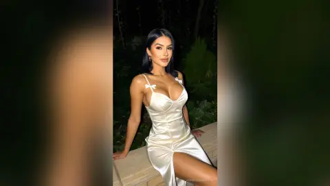 Glamorous woman in a white satin slip dress posing outdoors at night.