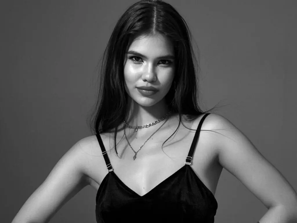 Portrait of a young woman in a black camisole and silver necklaces against a gray studio background.