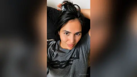 Smiling woman in a grey t-shirt relaxing indoors with a casual, cozy mood.