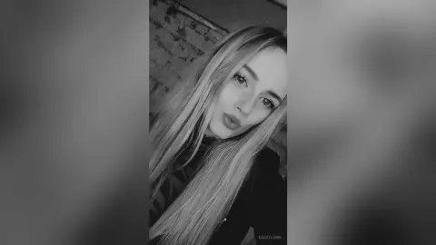 Close-up portrait of a blonde woman with long hair posing in a moody, black and white aesthetic.