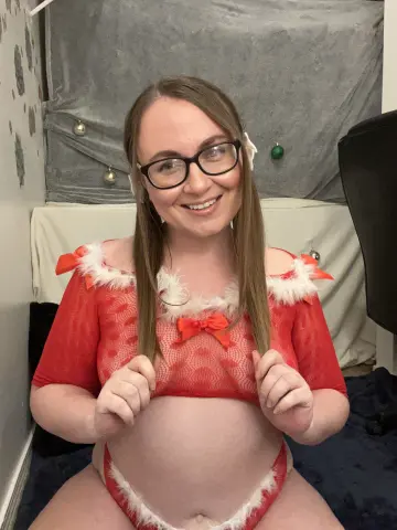 Smiling woman in a red and white festive Christmas outfit sitting in a cozy indoor setting.