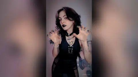 LorenLoiss poses in a black lace-up tank top with dark lipstick and dark hair, clawing at the air with her hands.