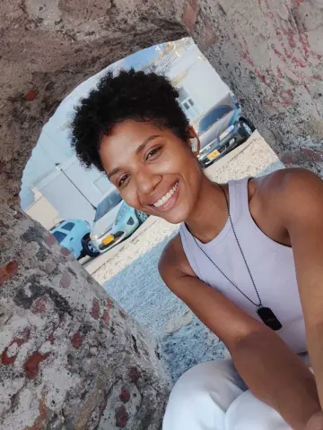 Smiling young woman in a white tank top enjoying a sunny day outdoors near urban buildings.
