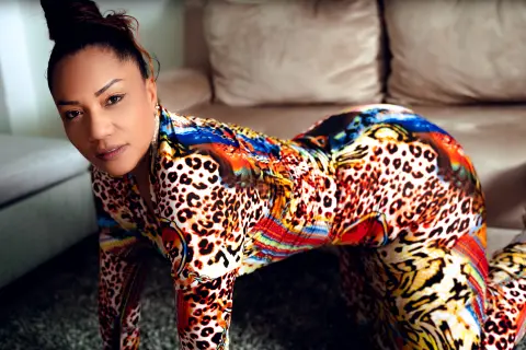 Confident woman in colorful leopard print jumpsuit posing on a living room floor.