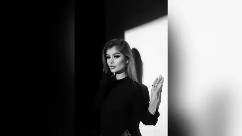 Moody black and white portrait of a glamorous woman in a black turtleneck against a dramatic shadow background.