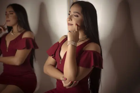 Elegant woman in a burgundy off-the-shoulder dress posing gracefully in a moody indoor setting.