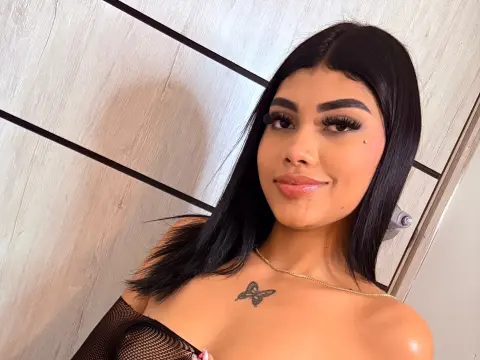 CherryLatinaGirl smiles at the camera with long dark hair and a butterfly tattoo on her chest.