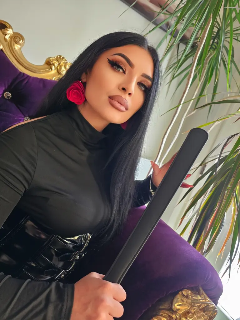 Woman with glamorous warm eyeshadow and nude lip makeup wearing a black blazer and floral neck accessory.