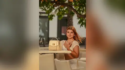 Smiling young woman in a white lace top sitting at an outdoor cafe on a sunny day.