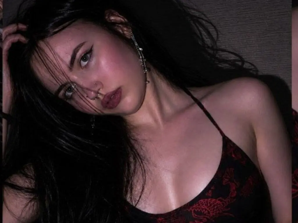 Young woman with long dark hair and nose ring wearing a black floral camisole in moody low light.