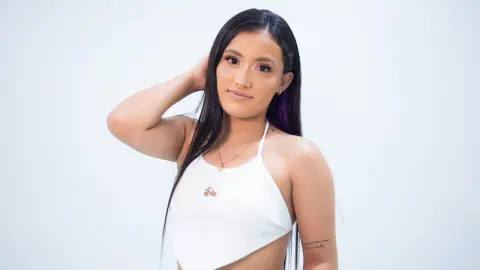 Young woman with long dark hair wearing a white ribbed halter top against a clean white background.