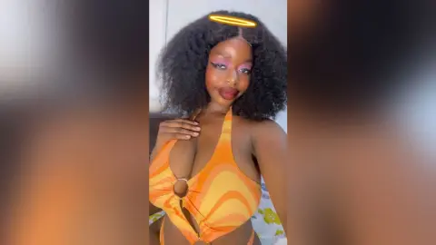Beautiful Black woman in an orange patterned halter swimsuit posing with a glowing halo headband.