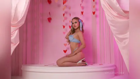 Blonde woman in light blue lingerie posing in a romantic pink room decorated with red heart decorations.