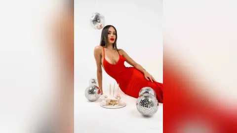 Glamorous woman in a red evening dress posing with disco balls for a festive New Year's Eve celebration.
