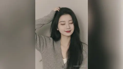 Smiling young woman with long dark hair wearing a cozy grey knit cardigan in a minimalist studio setting.