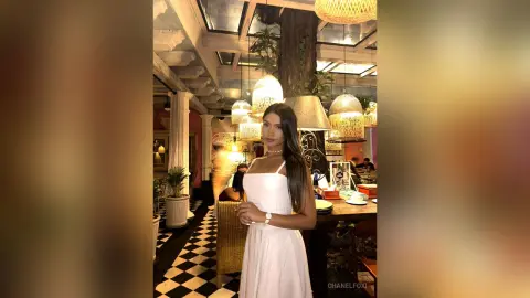 Young woman in a white summer dress standing in a chic restaurant with warm lighting and checkered floors.