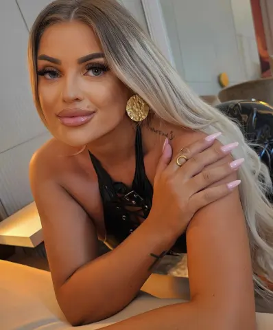 Blonde woman in a black halter top posing with a confident expression in a modern indoor setting.