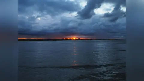 JessieLiu's photo shows a dark, cloudy sky over a wide body of water at sunset or sunrise.