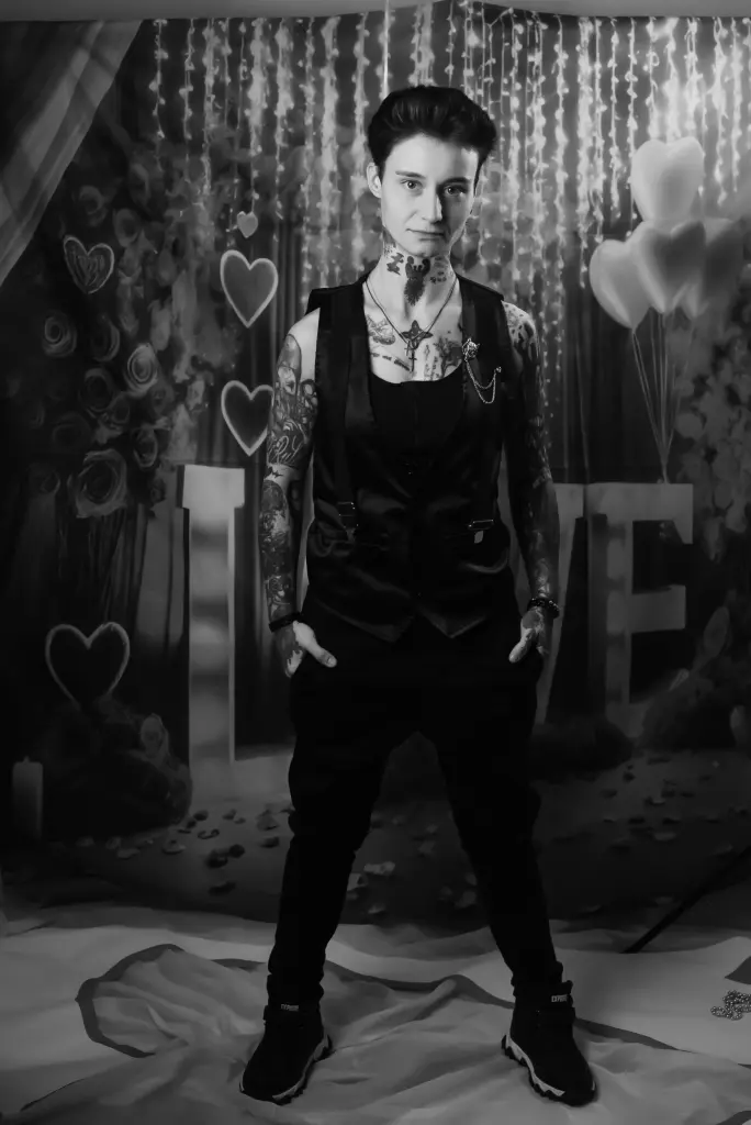 Kennyss poses in a dark setting, wearing a bow tie and holding a cigarette with smoke rising around her face.