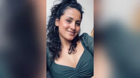 JulianaNavarro smiling with curly dark hair, wearing a low-cut dark green top while looking at the camera.