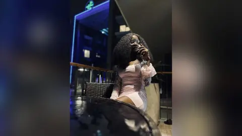 Elegant woman in a pink lace dress sipping a cocktail at a luxury rooftop lounge at night.