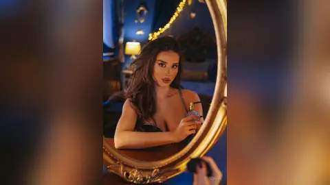 Beautiful woman in a black lace outfit applying perfume in a moody, dimly lit bedroom setting.