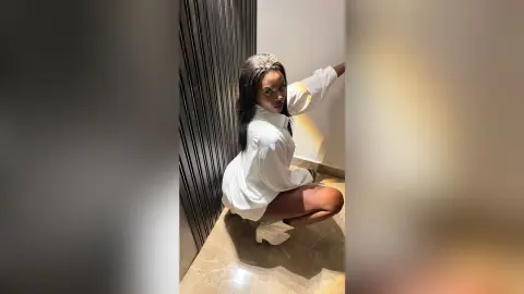 Elegant woman in a white button-down shirt and crown posing gracefully in a modern minimalist room.