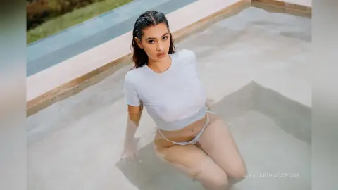 Young woman in a white t-shirt sitting in a shallow pool under bright sunlight.