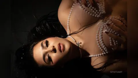 Glamorous woman with long dark hair wearing a luxury pearl necklace in a moody, cinematic setting.