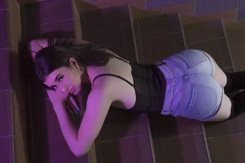 Young woman in black tank top and denim shorts lying on stairs under moody purple lighting.
