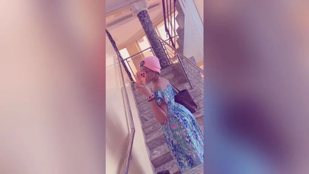 AlbertNina — AlbertNina takes a mirror selfie wearing a pink beanie and a blue floral patterned dress while standing on a staircase.