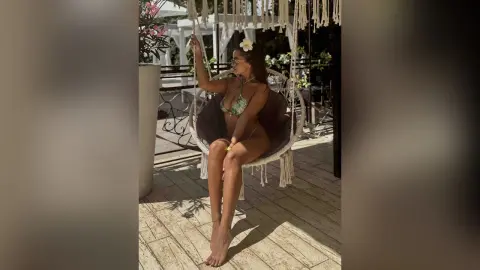 Woman in green bikini relaxing in a macrame hanging chair on a sunny outdoor patio.