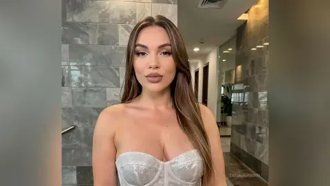 Beautiful woman in a white sparkly corset top posing in a modern marble bathroom setting.