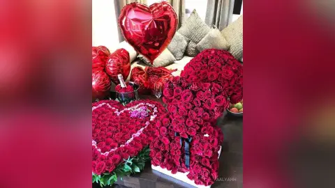 Aalyahh's photo features a large collection of red roses arranged in heart shapes, surrounded by red heart-shaped balloons and decorative pillows on a couch.