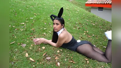 AmeliaStell wears a black bunny outfit and ears while lying on her stomach on a green grass lawn.