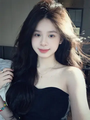 Young woman with long wavy hair wearing a black strapless top in a bright indoor setting.
