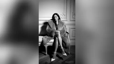Elegant woman in a luxurious faux fur coat sitting on a vintage sofa in a sophisticated black and white setting.