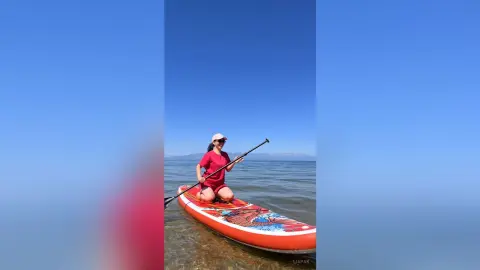 Woman in red athletic wear paddleboarding on a calm blue lake under a clear sunny sky.