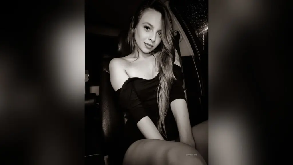 Smiling young woman in a white polka dot sheer top posing in soft natural indoor lighting.