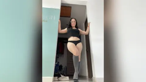 Woman in black crop top and briefs leaning against a doorway in a minimalist modern room.