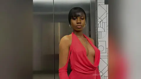 Elegant Black woman in a plunging red halter dress posing confidently in a modern elevator setting.